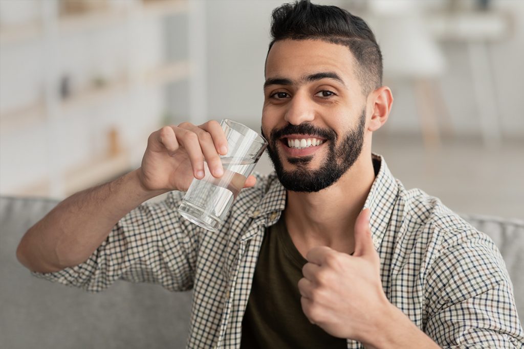 Person holding glass of water and doing a thumbs up